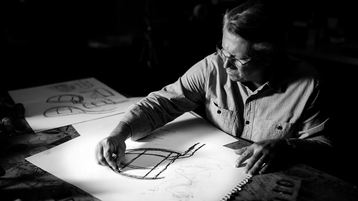 Black-and-white photo of Scotty Cameron sketching putter head designs in charcoal at a darkened studio table.