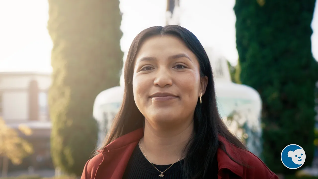 Smiling young woman with long dark hair in a red jacket stands outdoors with CHOC Research logo in the corner.