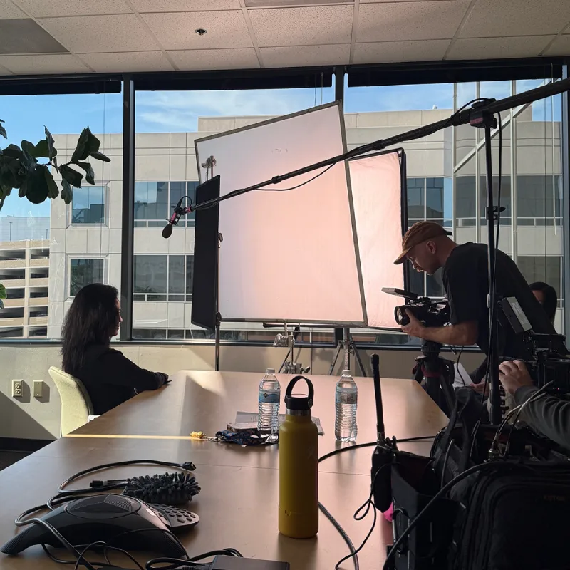 Behind-the-scenes of a video interview shoot in a conference room with camera, softbox light, and boom mic.