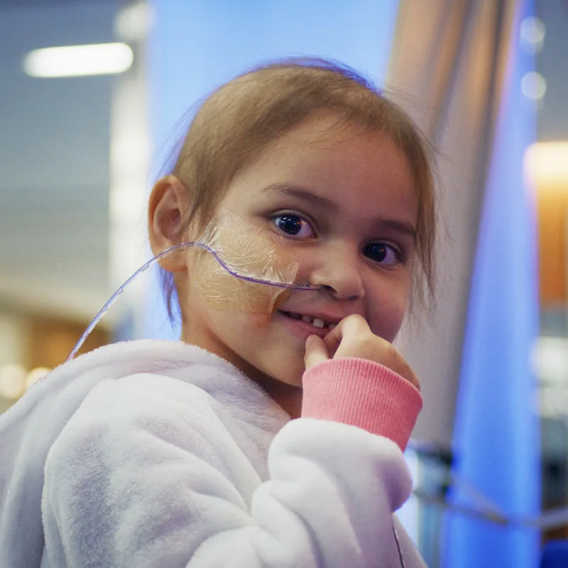 Young child with a nasal cannula smiles softly at the camera in a hospital setting. 