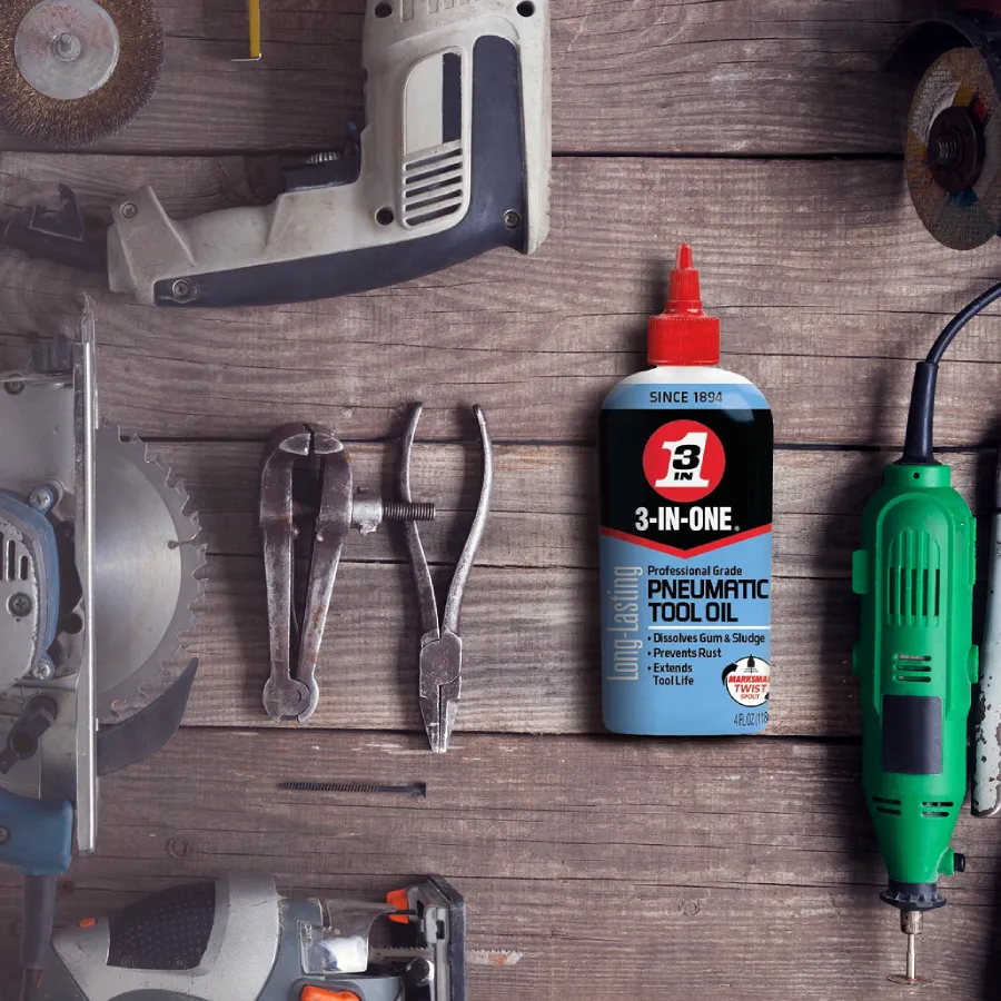 Bottle of 3-IN-ONE Professional Grade Pneumatic Tool Oil on weathered wood planks, surrounded by saws, pliers, and a rotary tool.