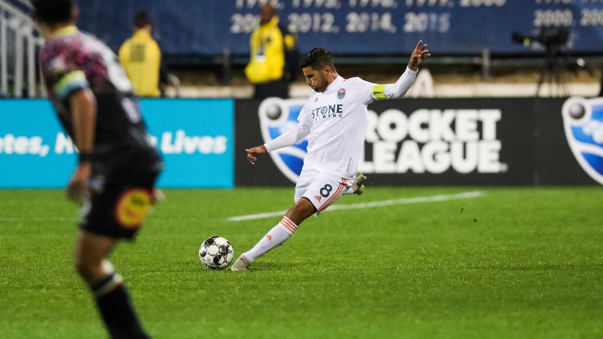 SD Loyal player in white home kit striking a soccer ball mid-match under stadium lights.