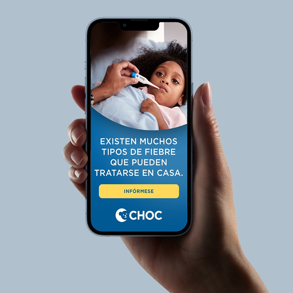 Hand holding phone showing CHOC Spanish-language ad: child having temperature taken with "Existen muchos tipos de fiebre que pueden tratarse en casa" and Infórmese button.