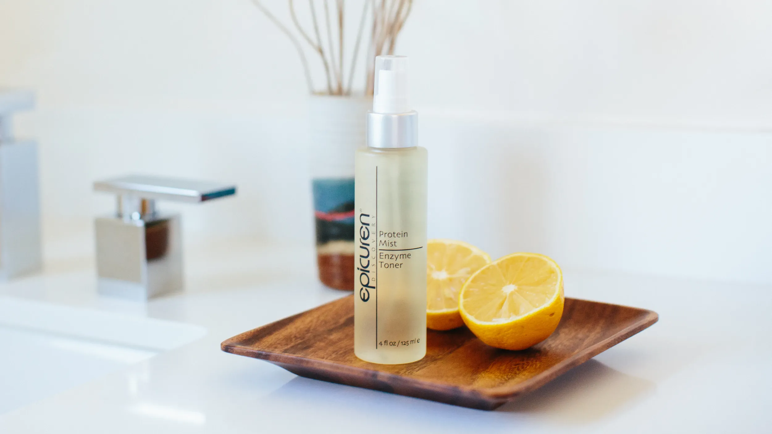 Epicuren Protein Mist Enzyme Toner bottle on a wood dish with sliced lemons in a bright bathroom setting