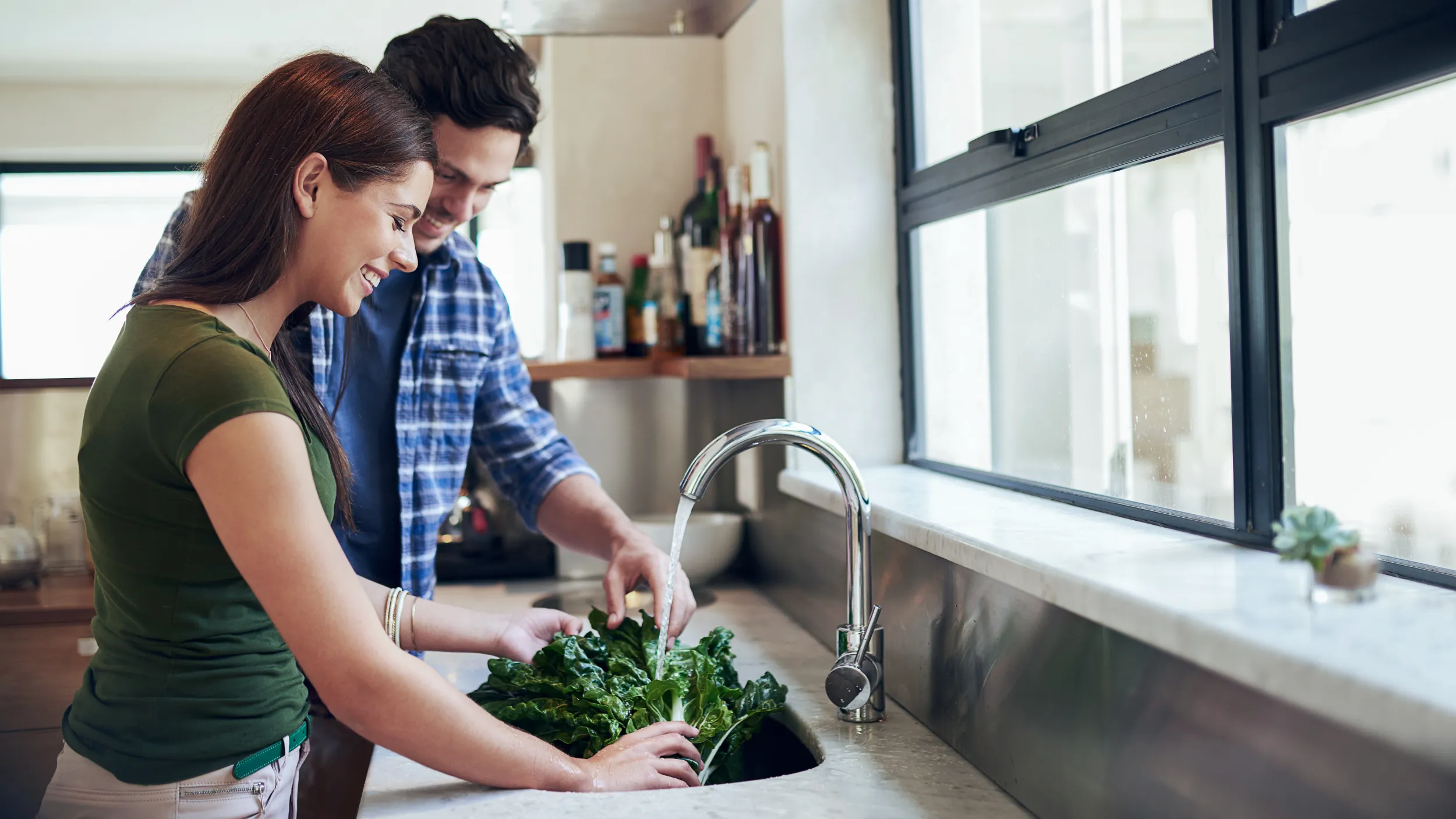 Smiling couple washing fresh leafy greens together at a kitchen sink with filtered water in a Shea Homes kitchen