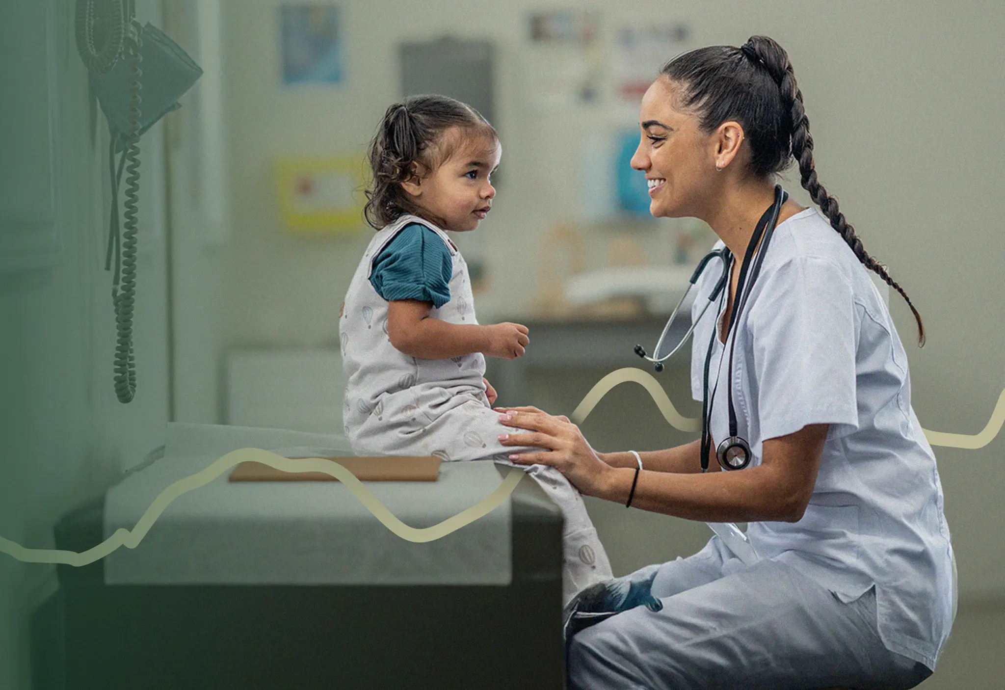 Nurse smiling at a toddler patient sitting on an exam table in a pediatric clinic room