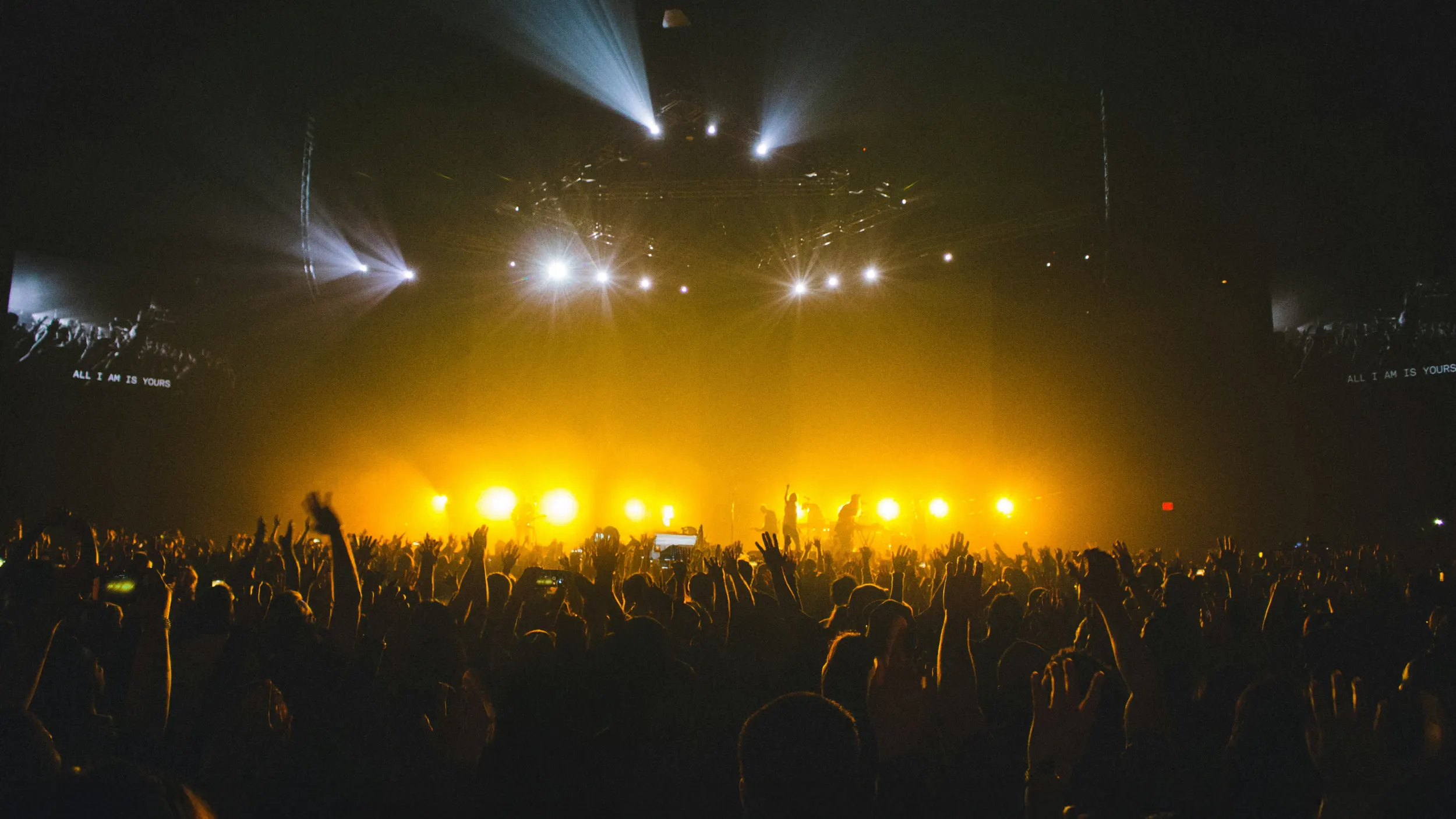 Crowd with raised hands at a concert under yellow and white stage lights