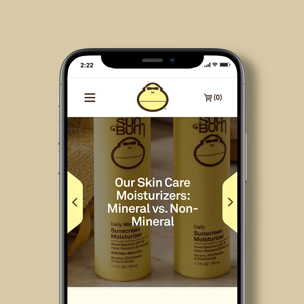 A smartphone showing the Sun Bum mobile website with a blog post titled 'Our Skin Care Moisturizers: Mineral vs. Non-Mineral,' with two Sun Bum sunscreen moisturizer bottles visible in the background.