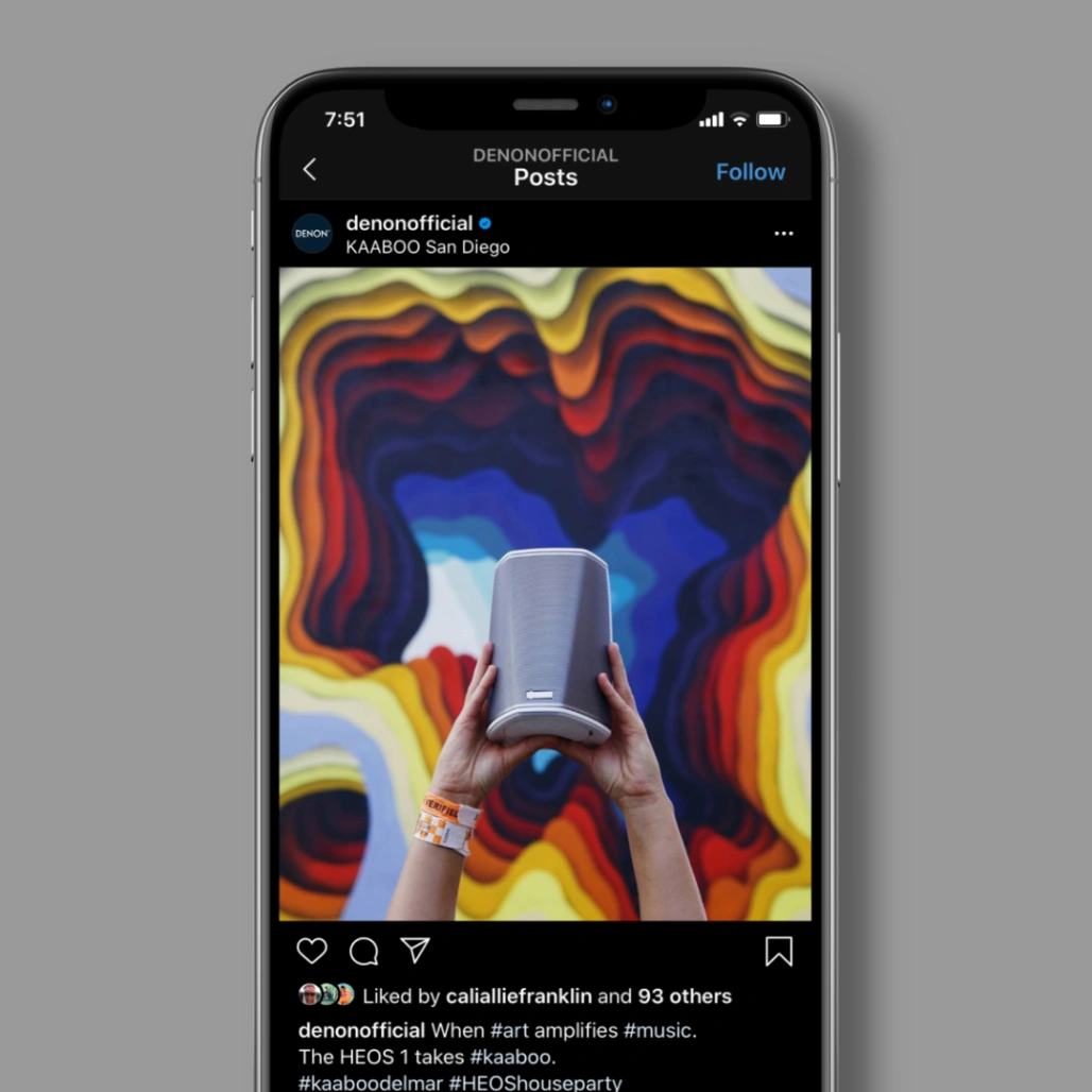 Phone screen showing Denon Instagram post of hands holding a HEOS 1 speaker against a colorful mural at KAABOO San Diego