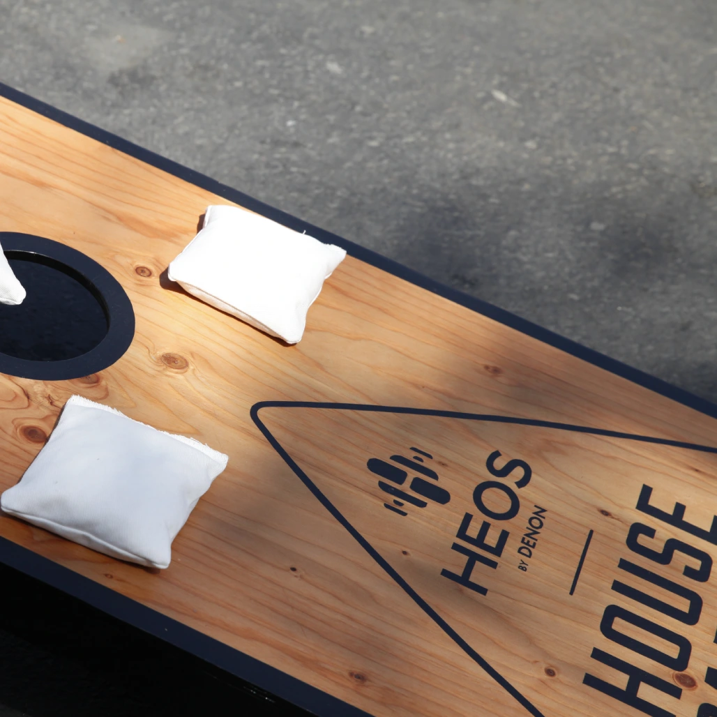 HEOS House Party branded cornhole board with white bean bags on a wood surface
