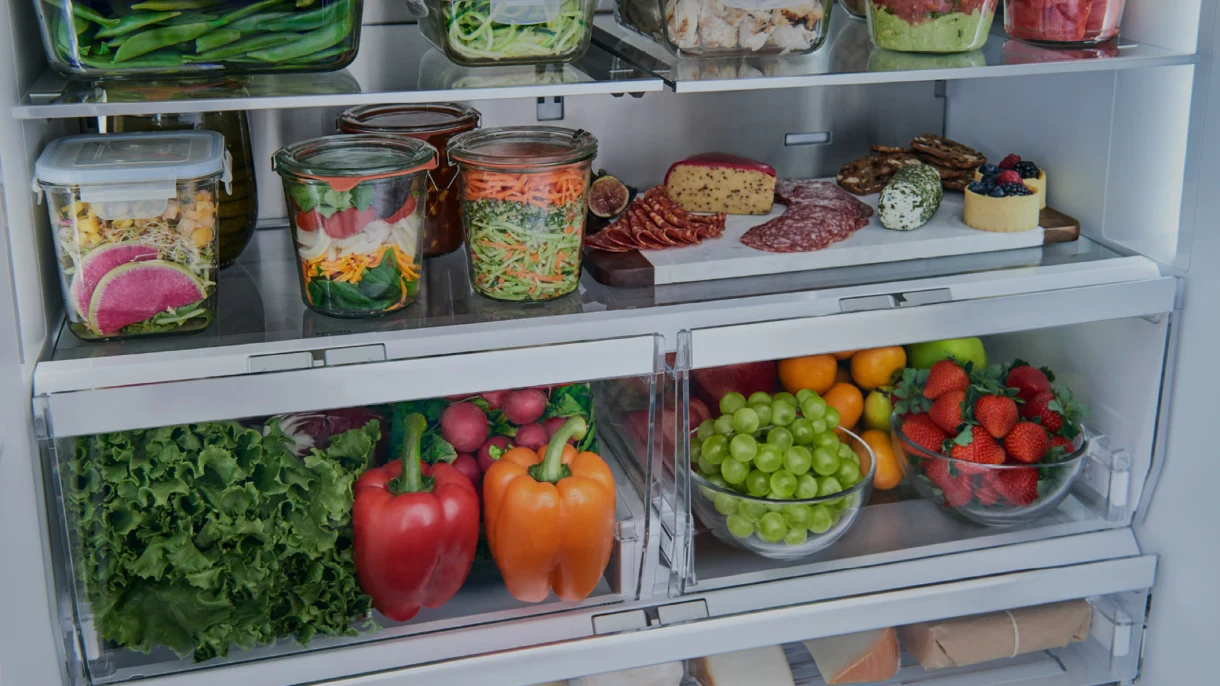 Inside of a Bosch refrigerator with clear drawers of fresh produce, glass jars of salads, and a charcuterie board