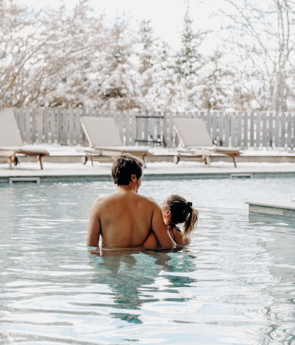 Couple dans la piscine extérieure chauffée entourée de neige aux Chalets du Mont d’Arbois — Megève.