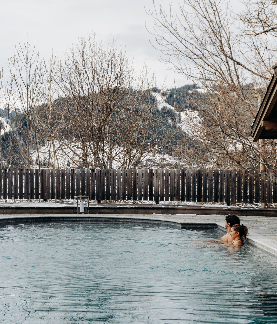 Couple profitant de la piscine extérieure chauffée avec vue sur les montagnes enneigées aux Chalets du Mont d’Arbois — Megève.
