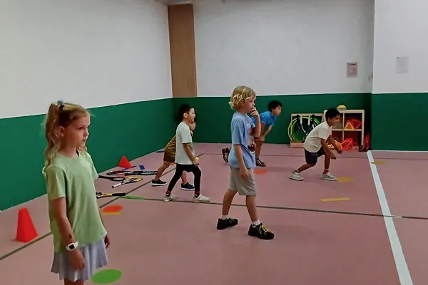 Kids playing tennis at holiday camp in indoor court.