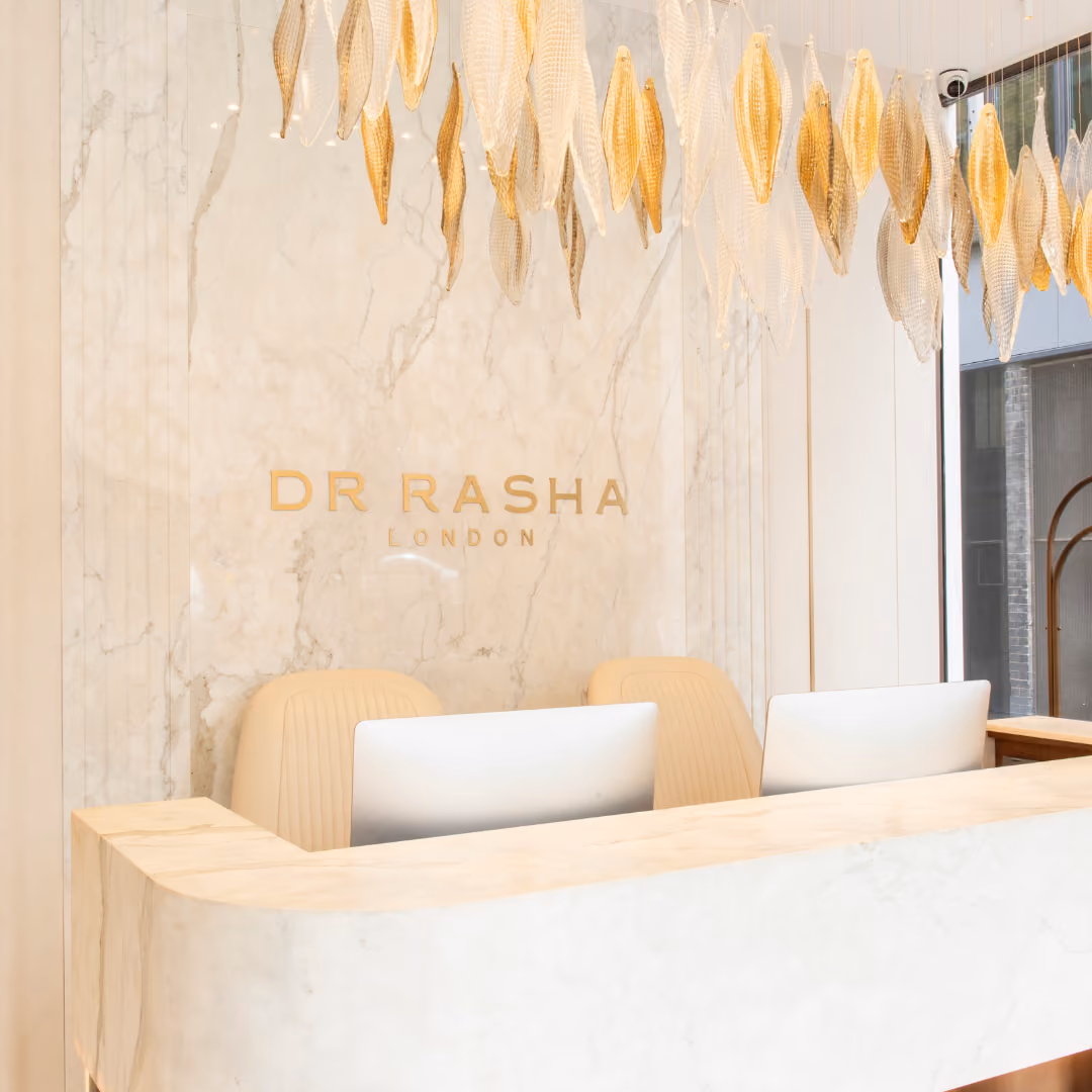 Modern reception desk with beige chairs and golden decorative leaves hanging above in a sleek clinic lobby.
