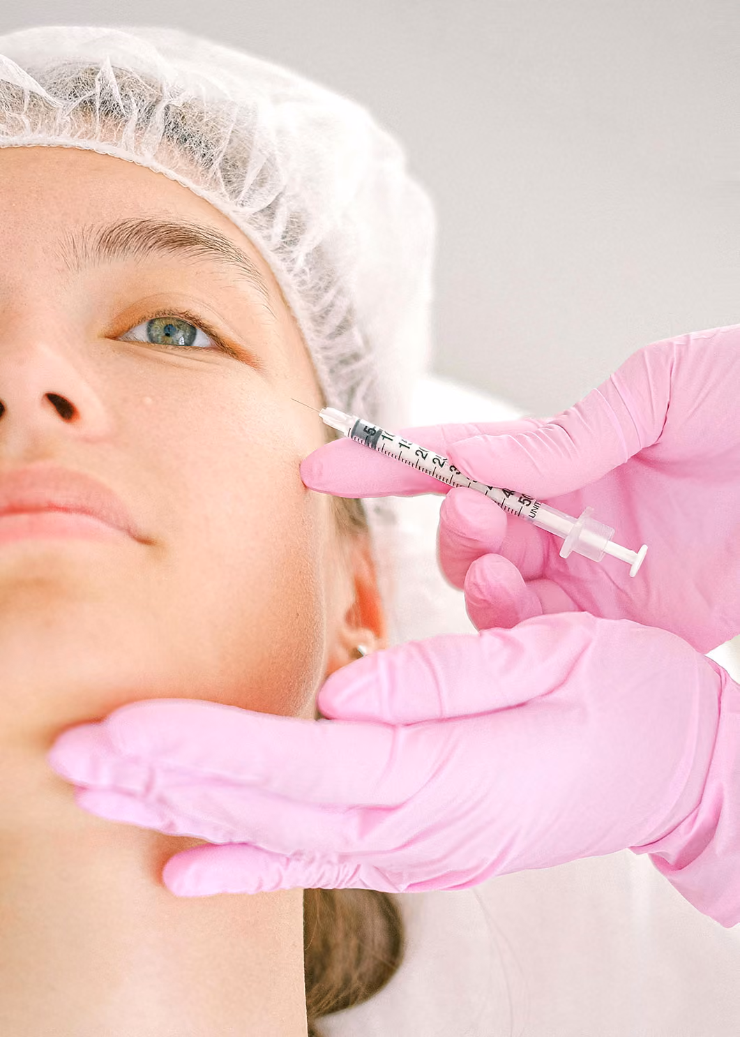 Person receiving cosmetic injection in the cheek from a gloved hand holding a syringe.