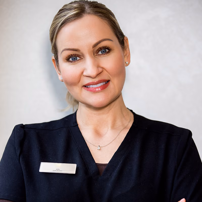 Smiling woman with blue eyes wearing a black shirt and name tag against a light background.