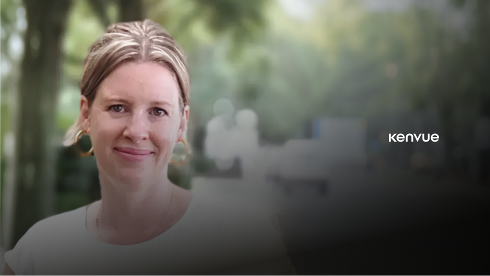 Smiling woman with long brown hair sitting against a textured gray wall with Danone logo on the left.
