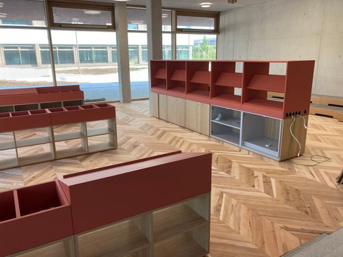 Innenraum mit Fischgrät-Holzboden, Regalen und großen Fenstern.