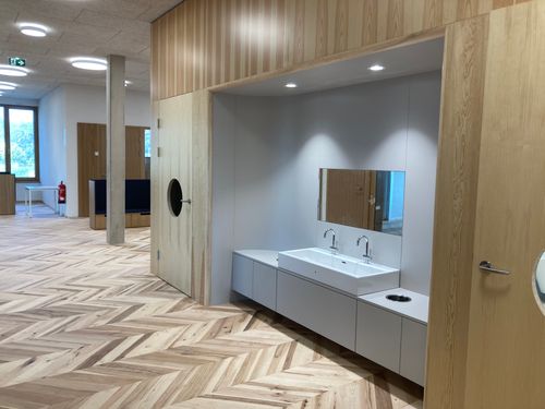 Innenraum mit Doppelwaschbecken, Spiegel, Holzfußboden und großen Fenstern.