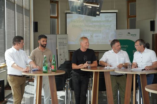 Fünf Männer stehen an Tischen und geben Interview