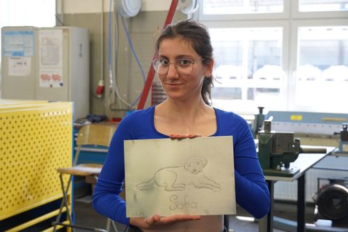 Person in blauem Langarmshirt hält eine Zeichnung eines liegenden Hundes mit dem Namen 'Sofia'