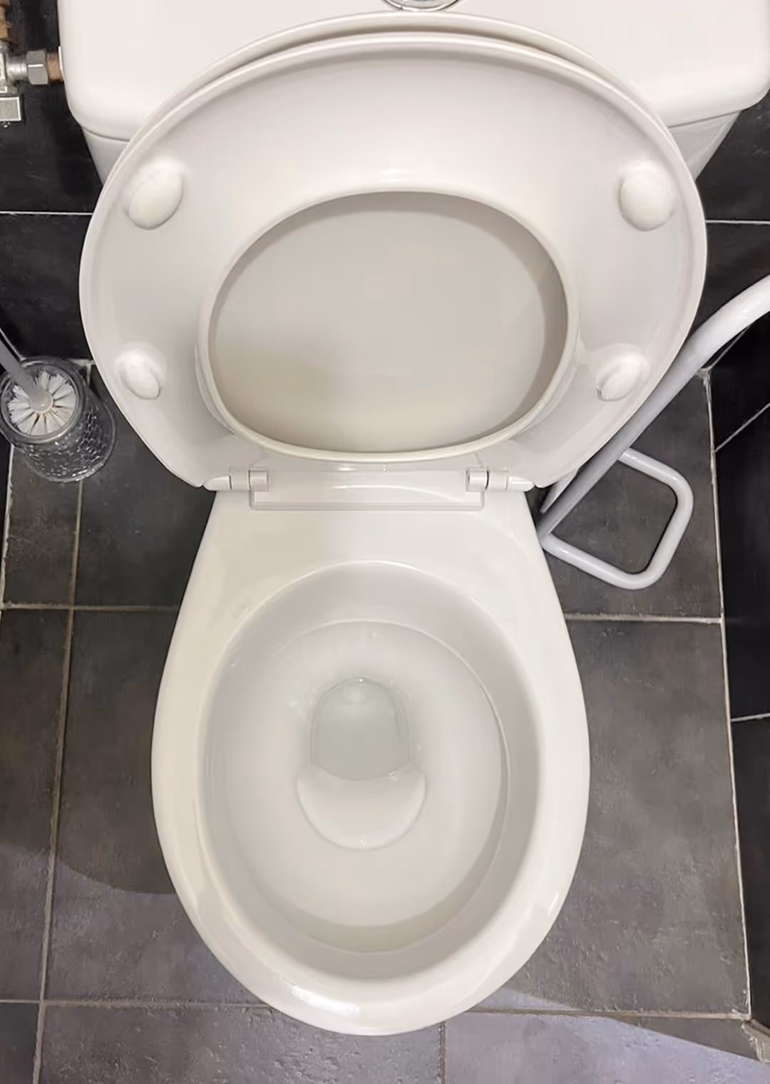 Top view of a clean white toilet with the lid and seat raised, positioned on dark grey tiled floor.
