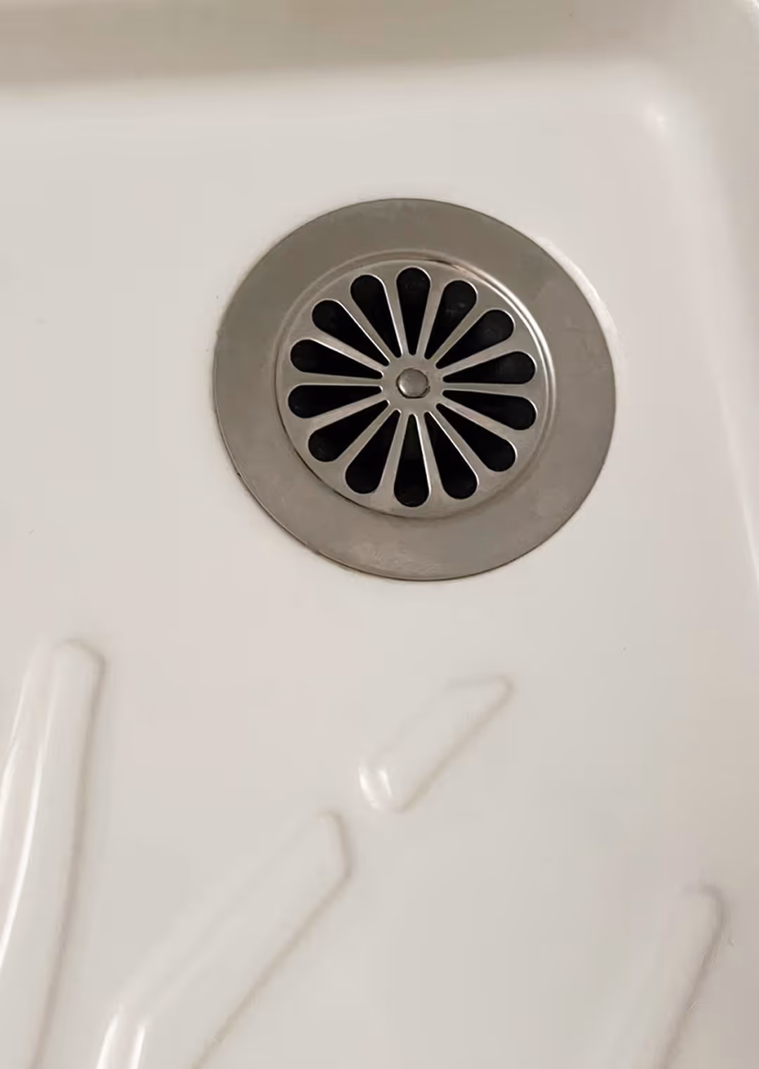 Close-up of a round metal drain cover with petal-shaped holes set in a white surface.
