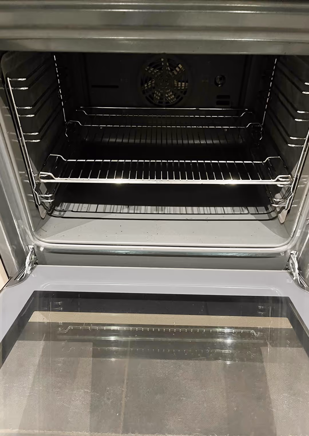 Empty stainless steel oven with the door open showing two wire racks and a fan at the back.