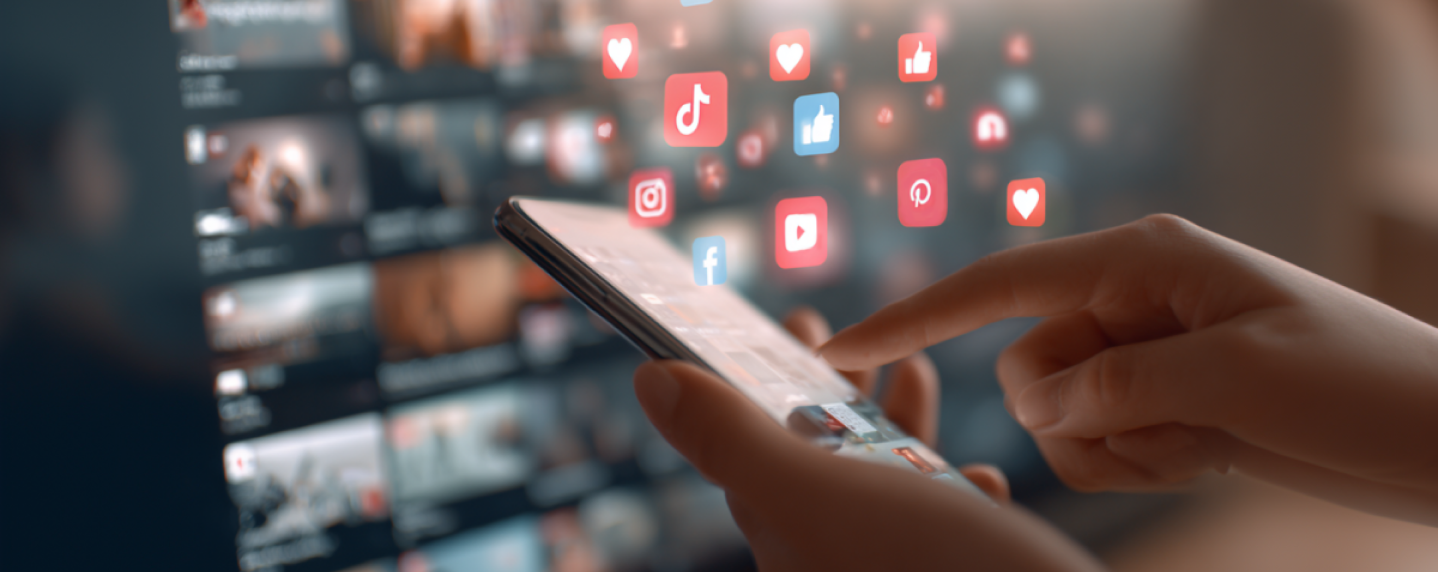 Person using a smartphone with social media icons like Facebook, TikTok, Instagram, and YouTube floating above the screen, representing social media advertising engagement