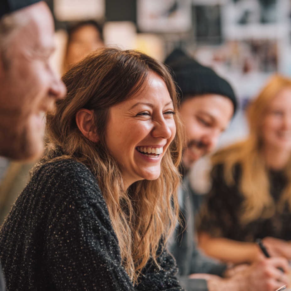Group of creative professionals smiling and collaborating in a bright, casual workspace, representing the energetic environment of a content agency.