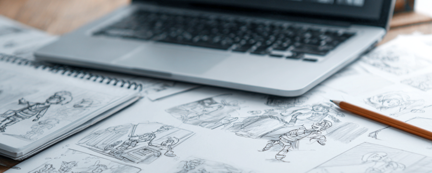 Storyboard sketches and character drawings laid out beside a laptop, representing the animation planning and design process