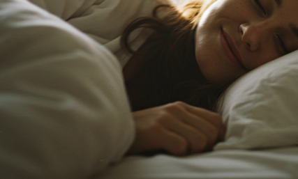 Woman peacefully sleeping in bed with a soft smile, wrapped in white bedding and natural morning light
