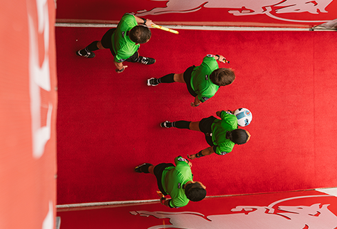 Overhead view of referees walking down a red carpeted tunnel, symbolizing murals and urban placements that create bold visual impact in sports marketing.