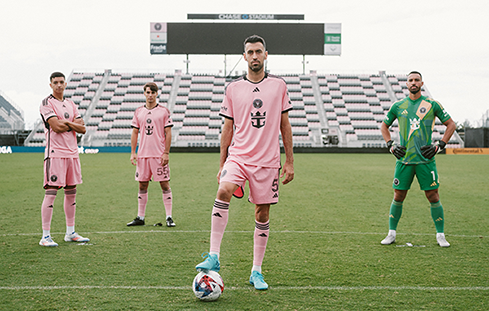 Soccer players in pink and green uniforms posing on the field, representing mobile tours and traveling activations that bring sports experiences to new audiences.