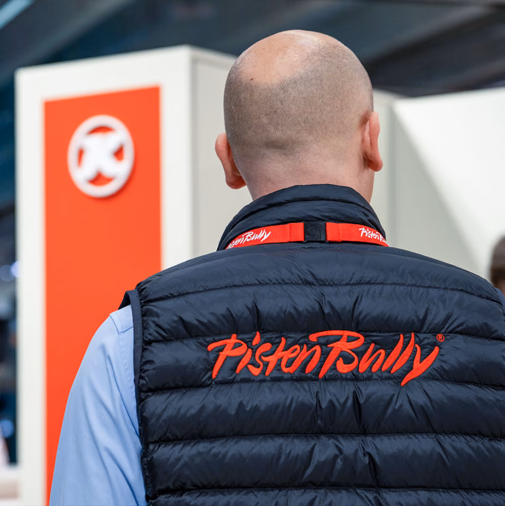 Rückansicht eines Mannes, der eine schwarze Weste mit roter „PistenBully”-Stickerei und einem passenden Schlüsselband trägt.