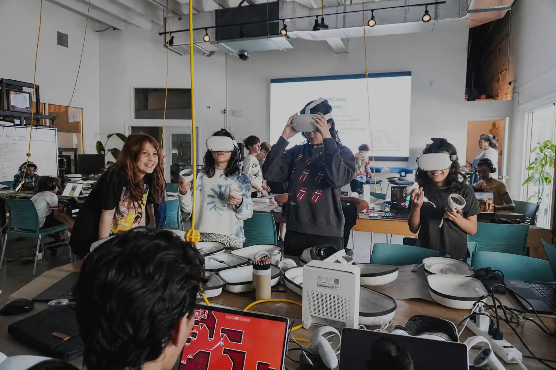 MUD Foundation XRCamp Winter 2025, featuring participants wearing virtual reality headsets and holding controllers during a workshop, surrounded by laptops, VR equipment, and interactive workstations in a bright classroom.