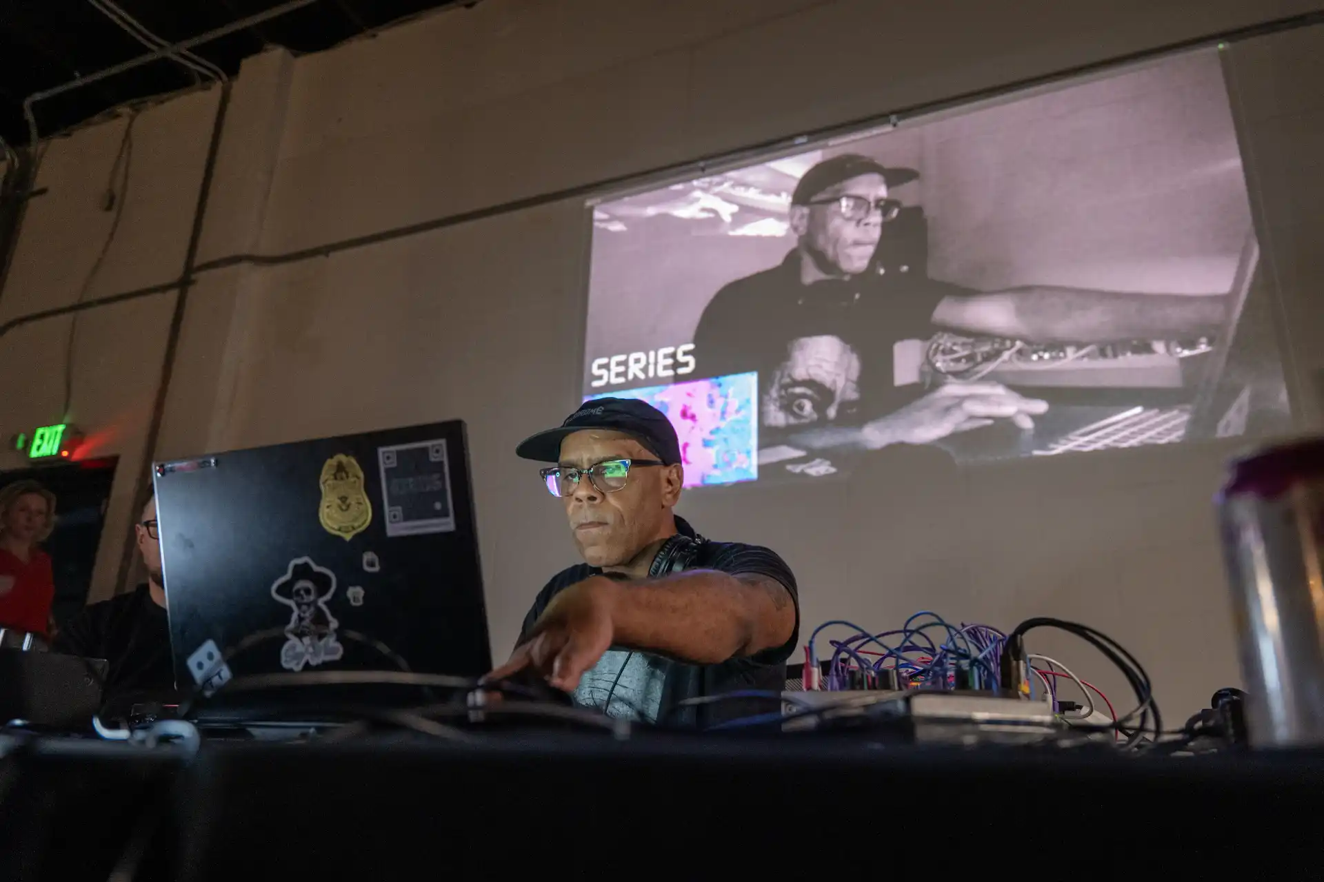 MUD Foundation The Sound of Art, featuring a musician operating electronic audio equipment and a laptop during a live performance, with a large projection displaying a black-and-white image and the word “SERIES” in the background.