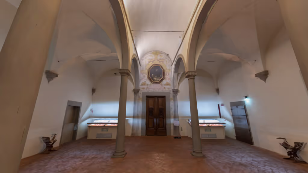 MUD Foundation Michelozzo’s San Marco Library in Verse, featuring a historic Renaissance interior with a terracotta floor, white vaulted ceiling, central stone columns supporting arches, wooden double doors, and illuminated display cases.