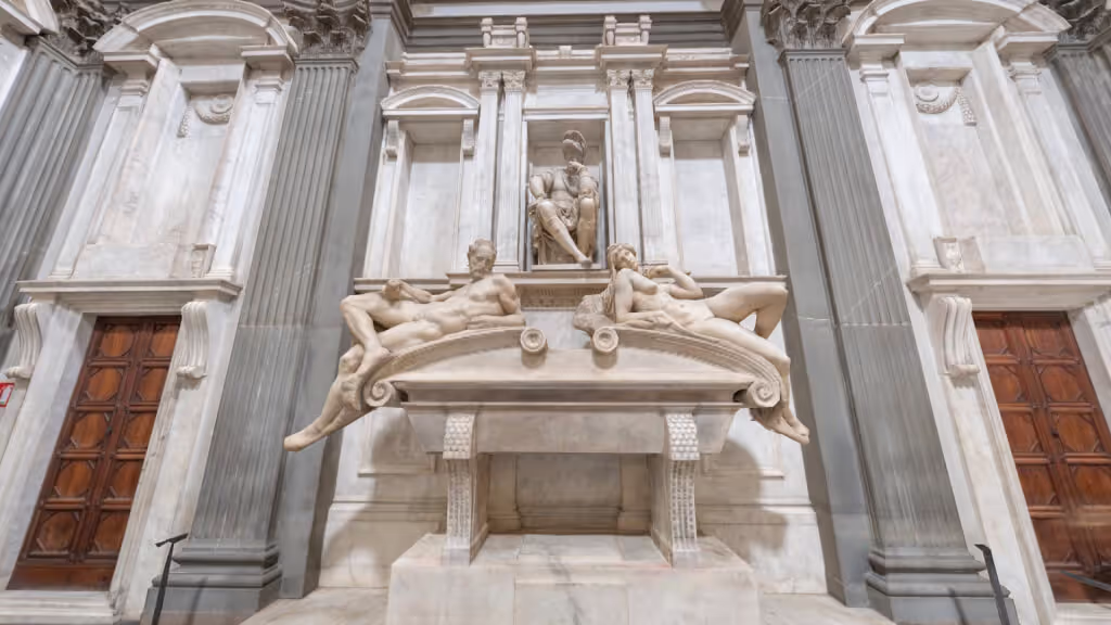 MUD Foundation Michelangelo’s New Sacristy in Verse, featuring a large white marble tomb with reclining male and female sculptures set within an ornate architectural niche, flanked by tall pilasters and wooden doors.