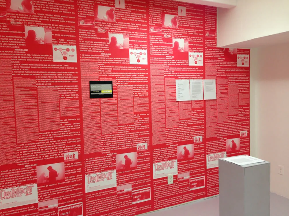 MUD Foundation Ernesto Oroza’s *Si despierta un pájaro intercambian sus cabezas los jugadores*, 2015, featuring a gallery installation covered with red text and printed materials, including diagrams, photographs, and a small video display.