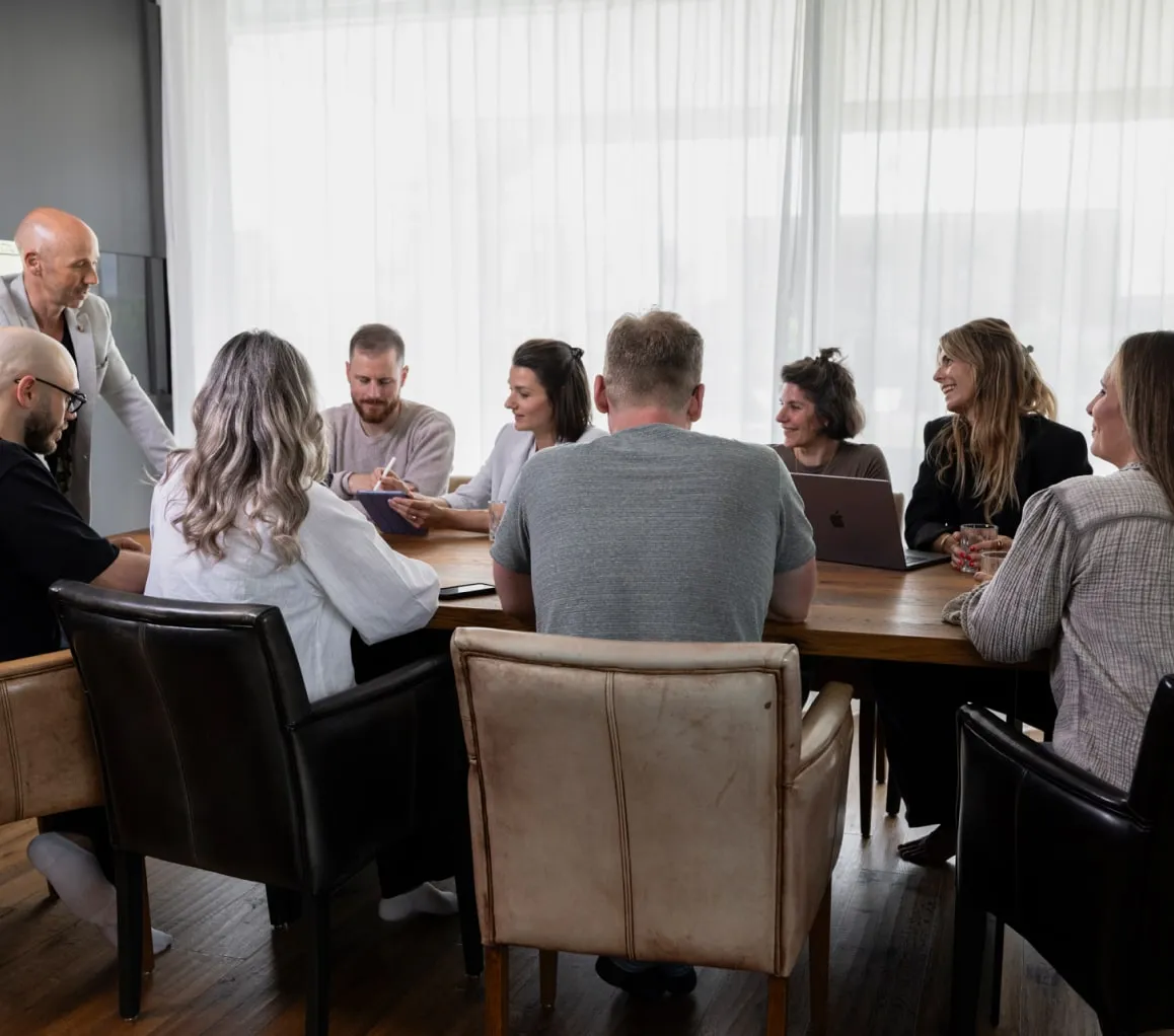 Eine Gruppe von Personen sitzt um einen Tisch und diskutiert Strategien zur Erstellung einer effektiven Präsentation mit Fokus auf E-Mail-Marketing