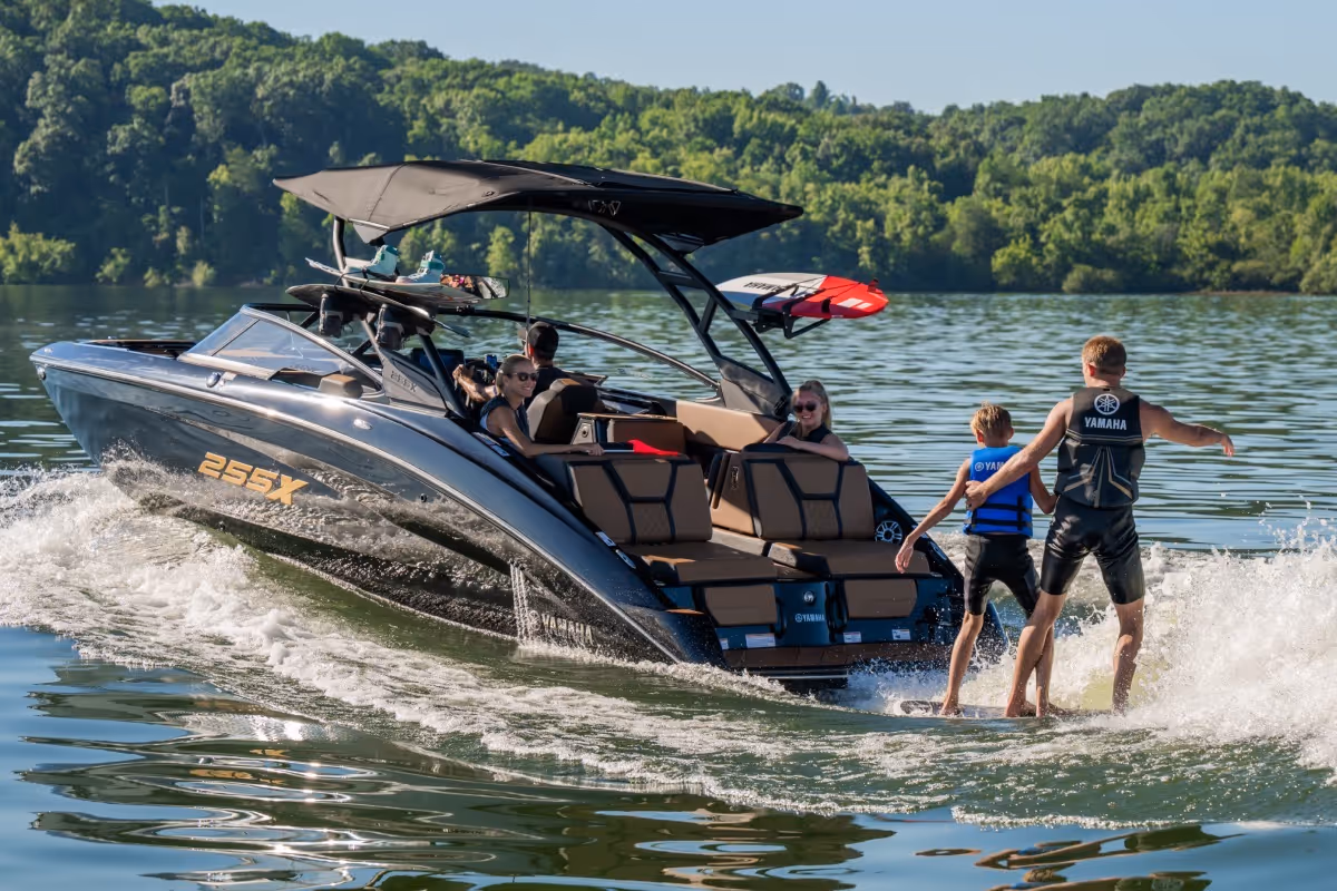 A sleek Yamaha 255X speedboat on a lake with two people waterskiing behind and others relaxing inside the boat.