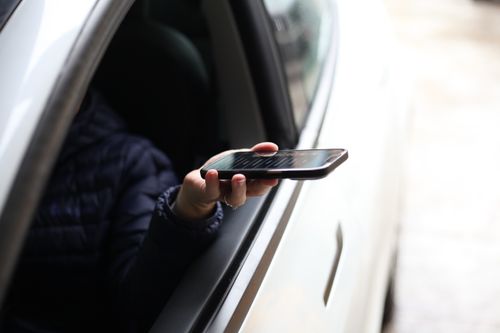 A woman reaching her phone out of a car window at a drive thru.