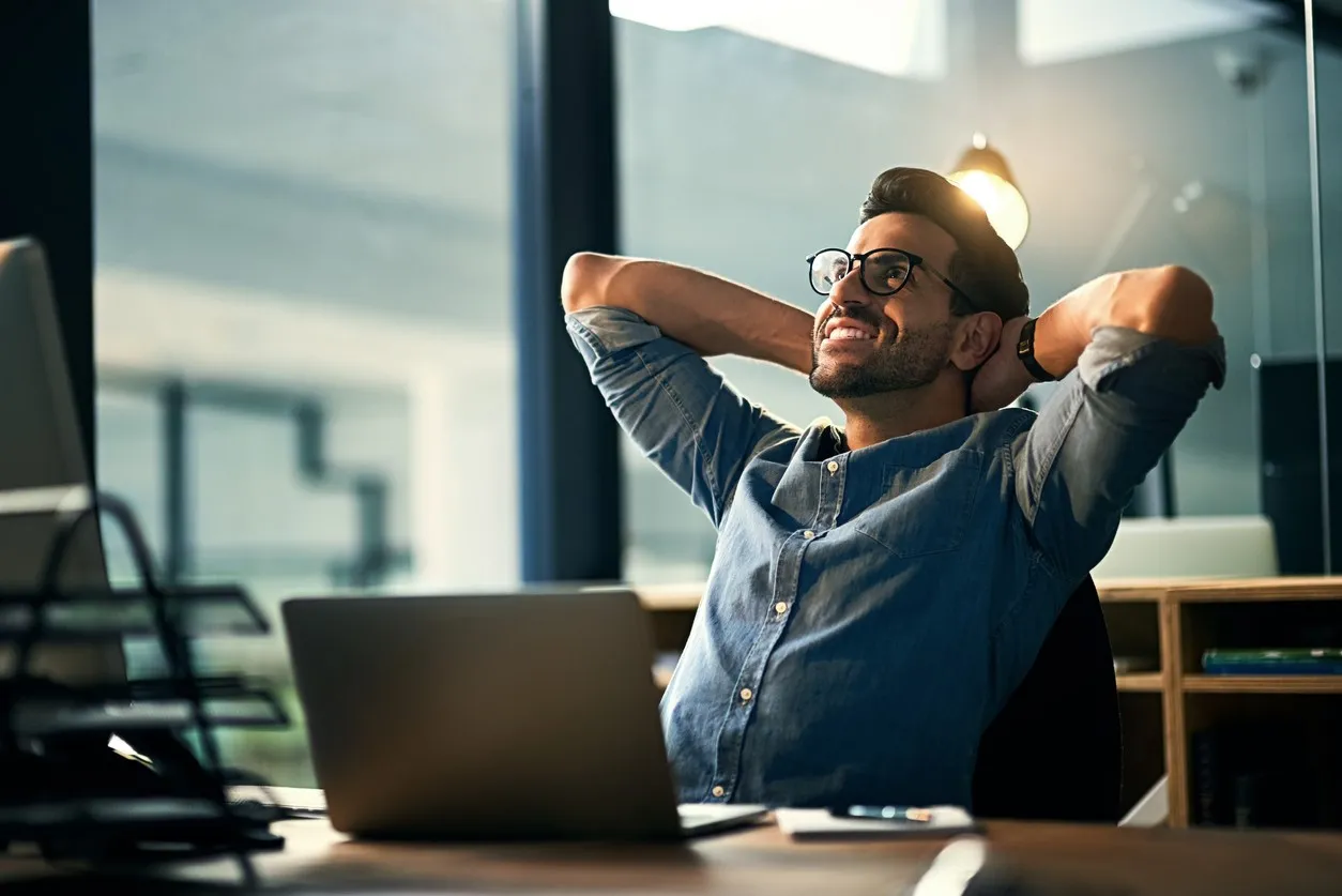 A man in a blue shirt is sitting at a desk with a laptop.