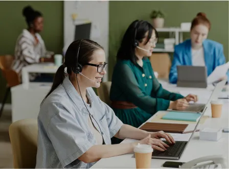 A woman wearing a headset and glasses is typing on a laptop.