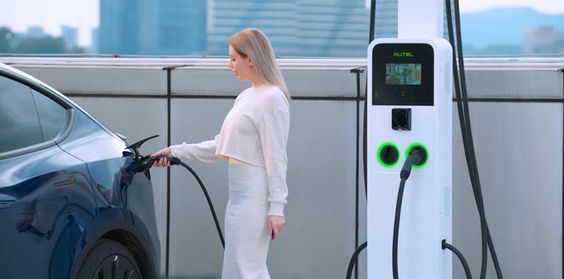 A woman plugging in her electric vehicle using an Autel commercial EV charger