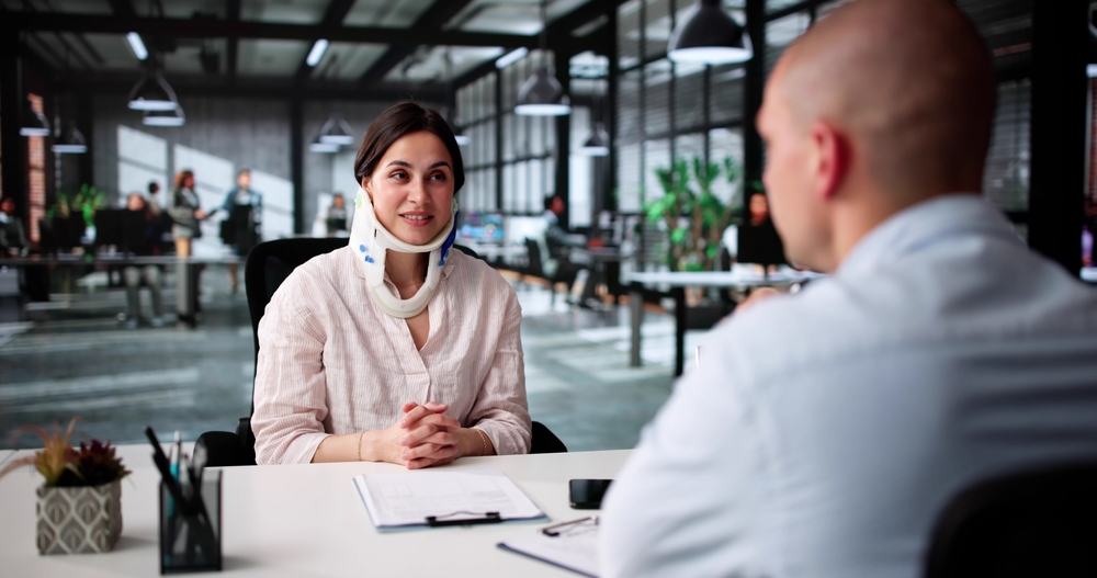 Personal injury client wearing a neck brace discussing a legal case with an attorney in a professional law office setting.