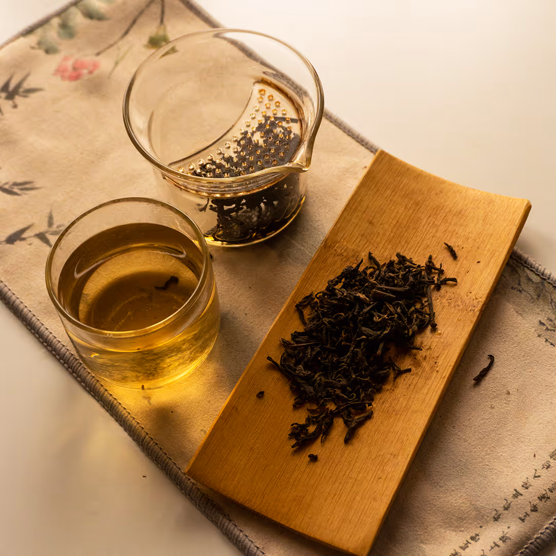 Tè fermentato con foglie di tè secche su un vassoio, una tazza di tè e un contenitore di vetro.