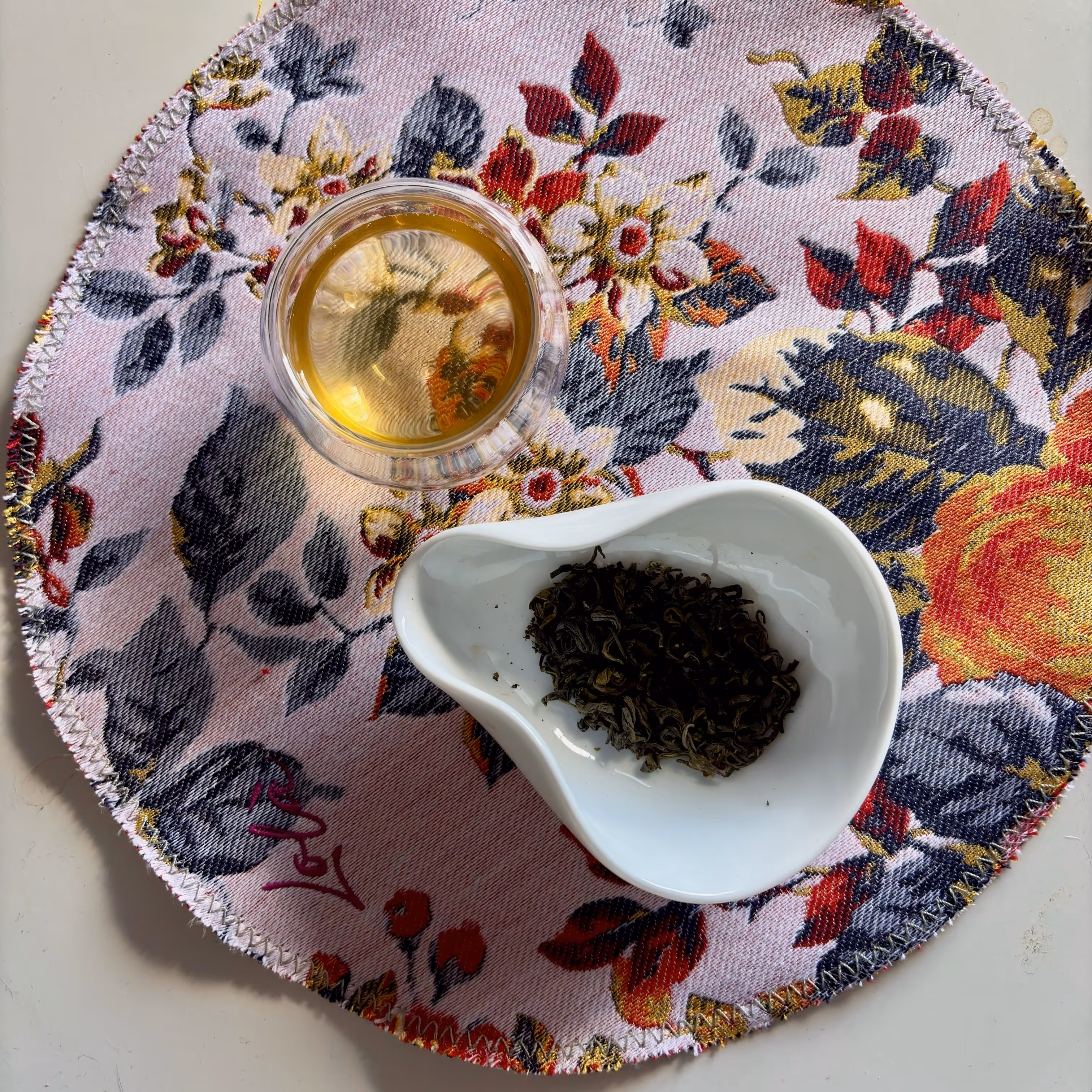 Tazza di tè e foglie di tè secche in una ciotola bianca su un tovagliolo floreale.
